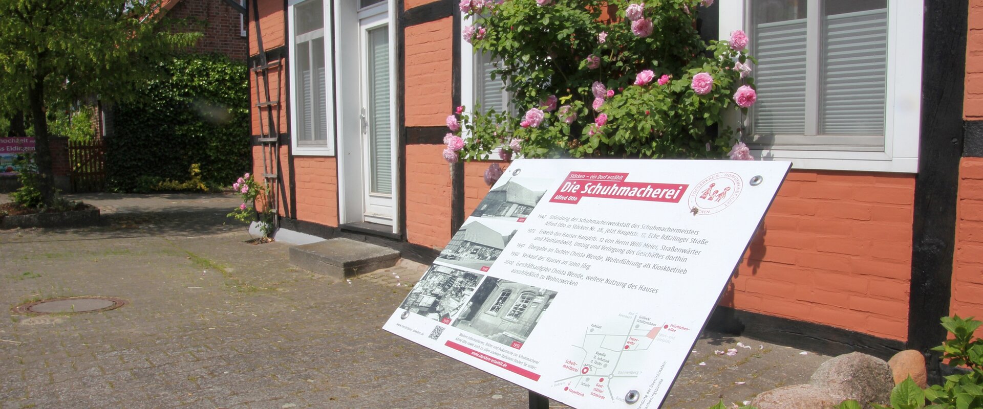 Blick auf eine Infotafel zur Geschichte des dahinter befindlichen Schumacher-Hauses in Stöcken / Landkreis Uelzen