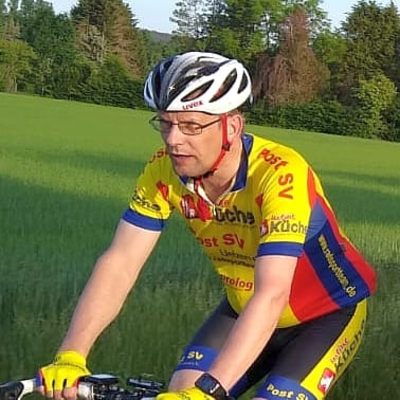 Ein sommerlich gekleideter Radsportler fährt auf einem Rennrad durch ein Feld.