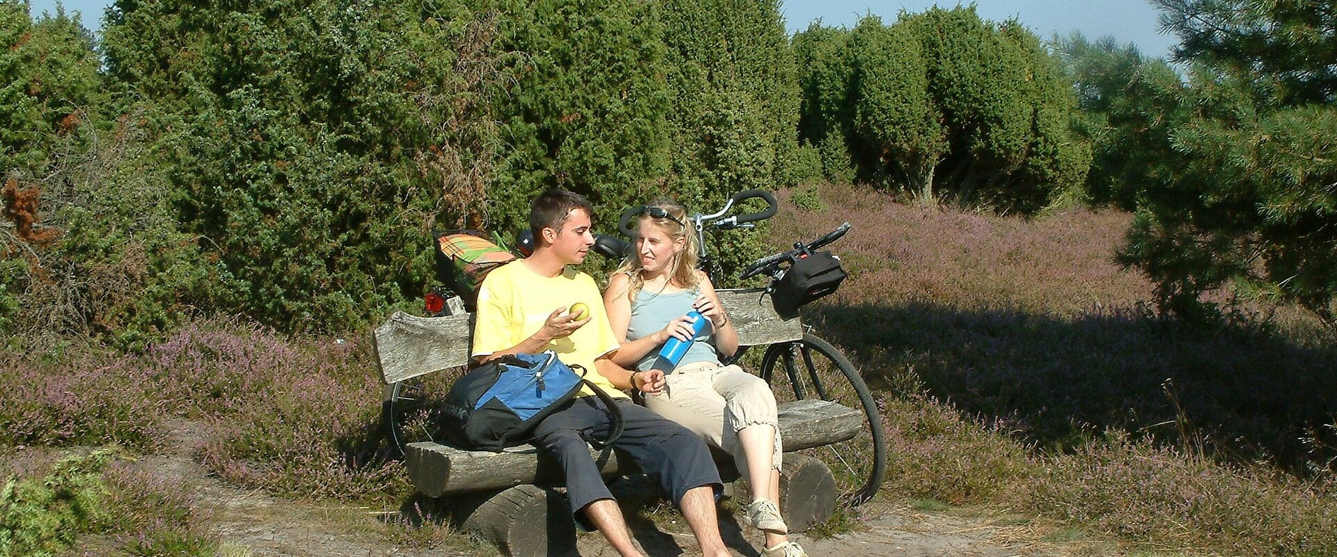 Ein junges Paar rastet auf seiner Fahrradtour auf einer Bank in der blühenden Ellerndorfer Wacholderheide.