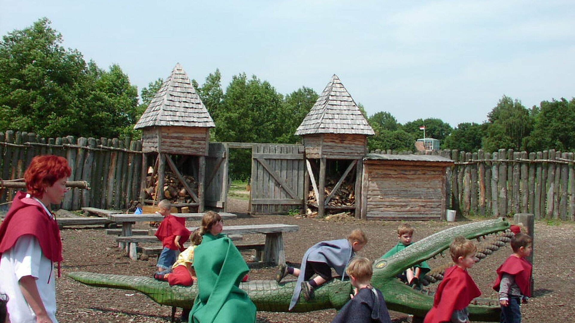Eine Gruppe mittelalterlich gewandeter Kinder spielt in Begleitung einer Museumspädagogin im Robin-Hood-Castell (einer nachempfundenen, aus Holz erbauten, mittelalterlichen Befestigungsanlage)