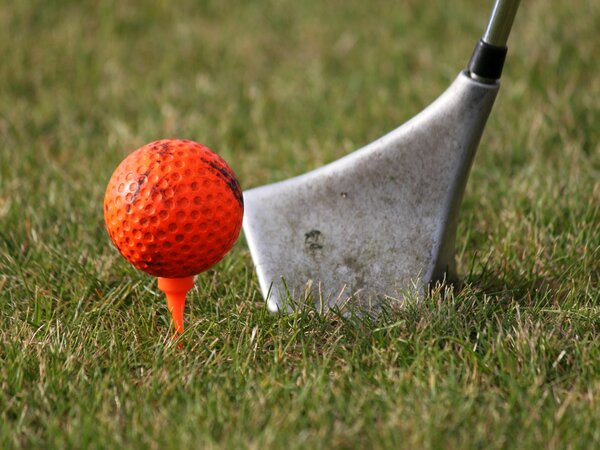 Detailaufnahme eines Swingolf-Schlägerkopfes neben einem roten Golfball auf einer Rasenfläche