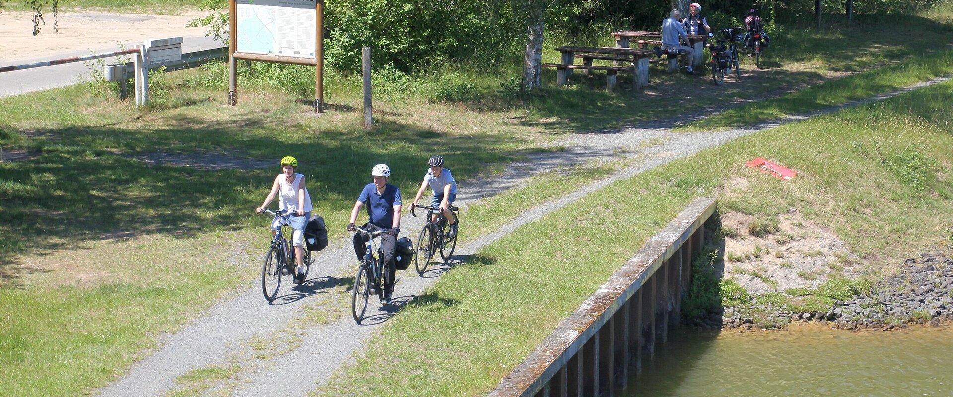 Eine Familie fährt mit ihren Fahrrädern entlang des Weser-Harz-Heide-Radwegs auf dem geschotterten Kontrollweg des Elbe-Seitenkanals.