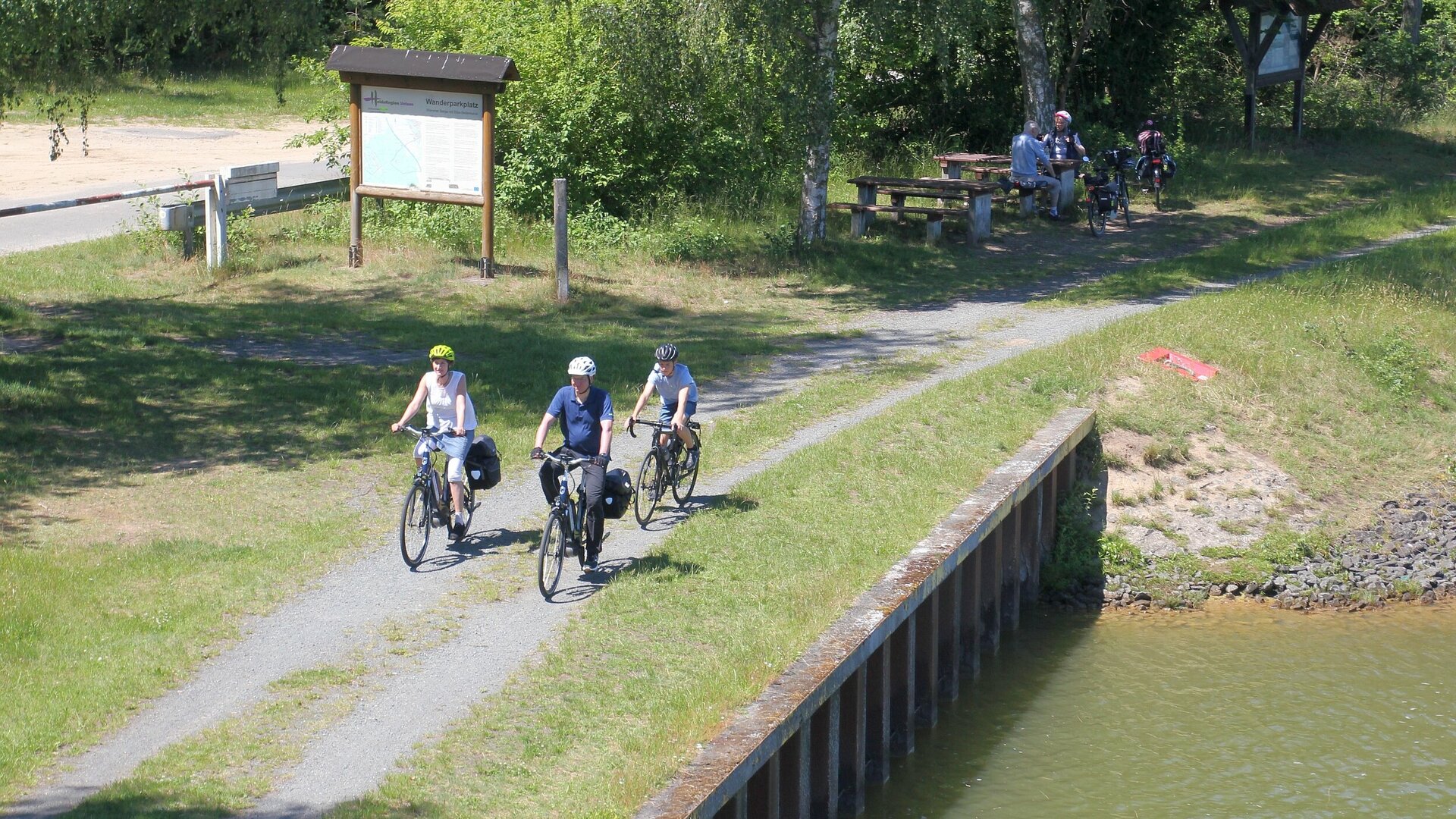 Eine Familie fährt mit ihren Fahrrädern entlang des Weser-Harz-Heide-Radwegs auf dem geschotterten Kontrollweg des Elbe-Seitenkanals.