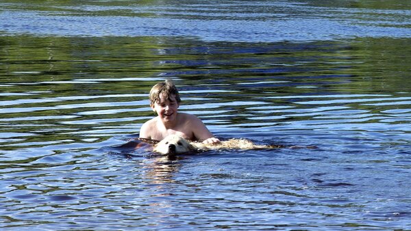 Ein Junge badet mit seinem Hund in einem Gewässer
