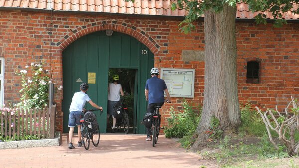 Eine Familie mit Fahrrädern durchquert das Eingangstor des Klosters Ebstorf.