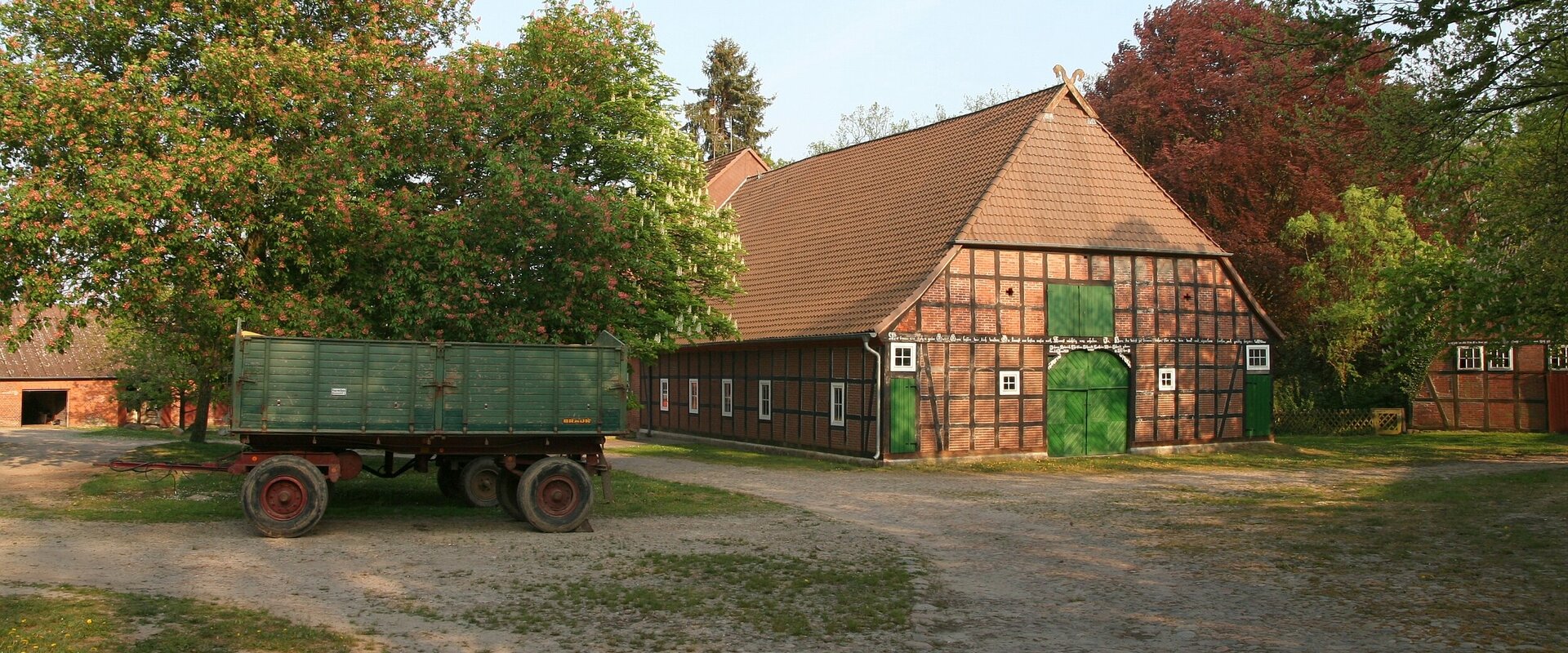 Hofanlage / Bauernhof in Wessenstedt mit großem Hallenhaus in Fachwerk-Bauweise und schräg davor parkendem Gummiwagen (Anhänger)