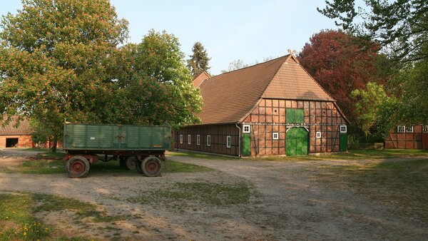Hofanlage / Bauernhof in Wessenstedt mit großem Hallenhaus in Fachwerk-Bauweise und schräg davor parkendem Gummiwagen (Anhänger)